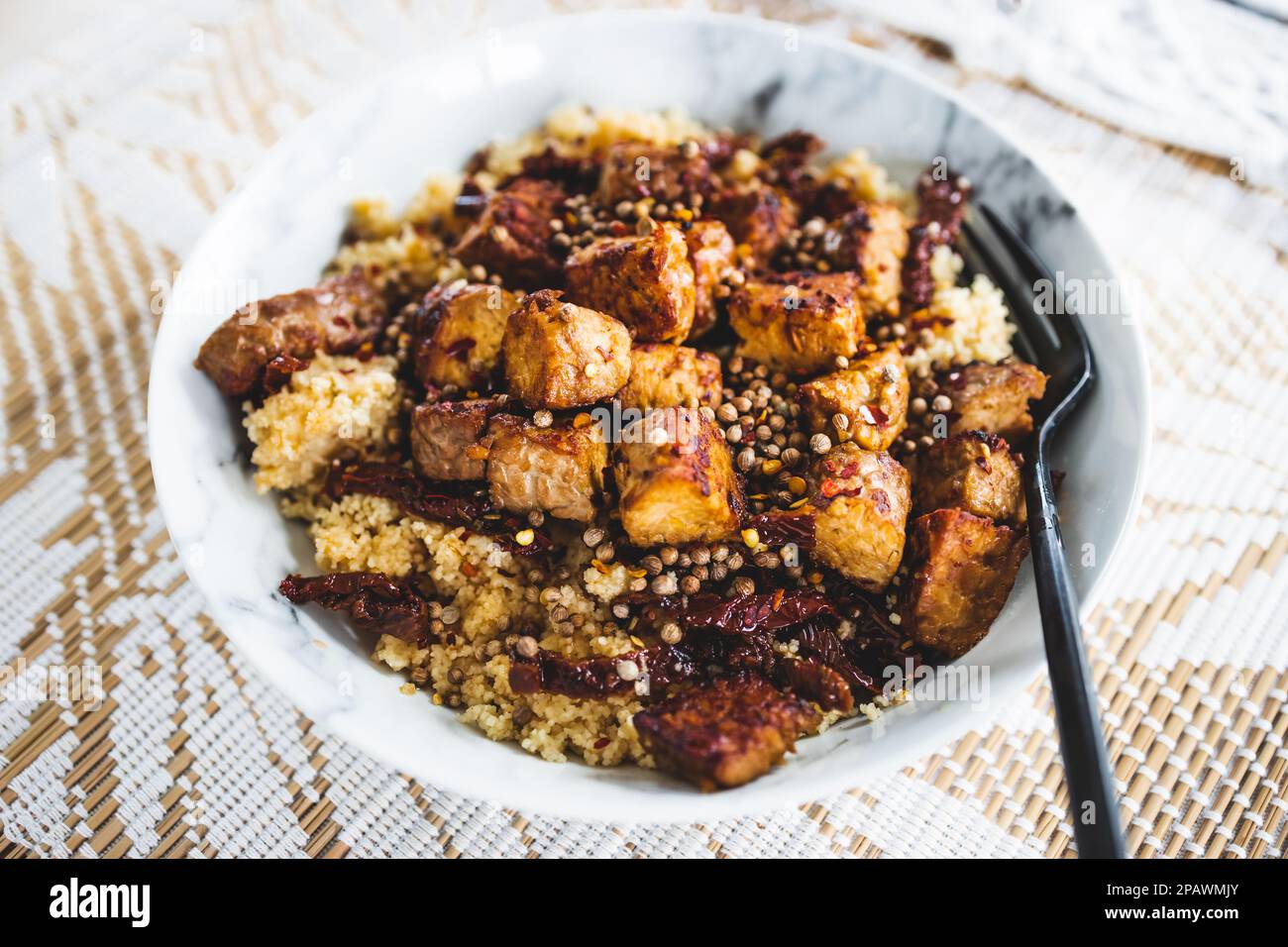 plant-based couscous with grilled tempeh cubes topped with chilli flkes and coiander seeds, healthy vegan food recipes Stock Photo
