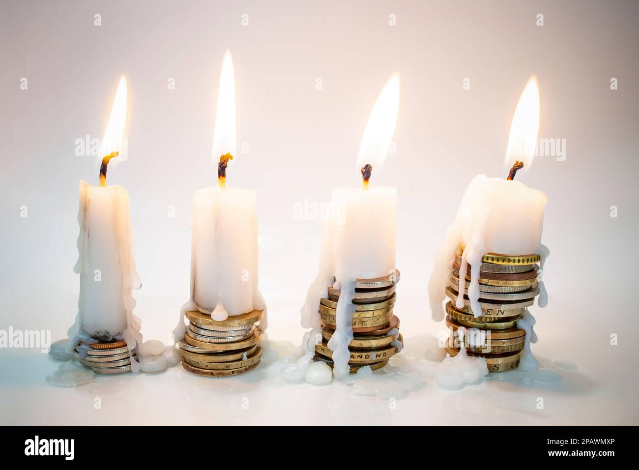 white candles burning on top on coin stacks, on gray background. More