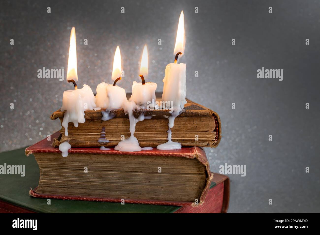 4 burning candles with dripping wax on vintage hard cover books, soft focus close up Stock Photo