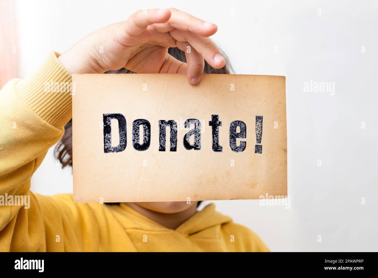 Child hand holding a piece of paper with the word Donate! stamped with black ink, close up Stock Photo