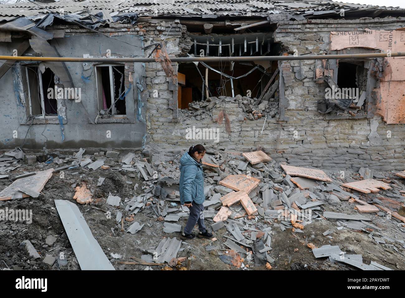A woman walks past a house destroyed in recent shelling in the course of Russia-Ukraine conflict in Donetsk, Russian-controlled Ukraine, March 12, 2023. REUTERS/Alexander Ermochenko Stock Photo