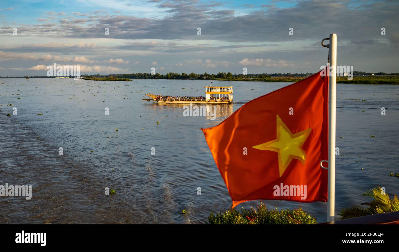 A crowded river ferryboat crosses the Mekong River past a Vietnamese