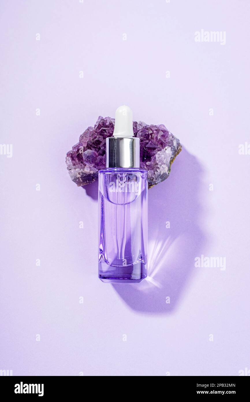 Purple cosmetic serum bottle on amethyst crystal stone. Top view, close up. Stock Photo