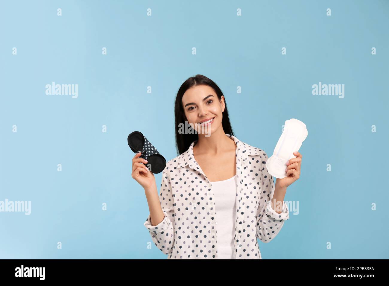 Young woman with reusable and disposable menstrual pads on light blue ...