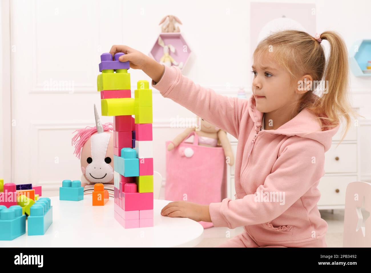 Cute little girl playing with colorful building blocks at table in room ...