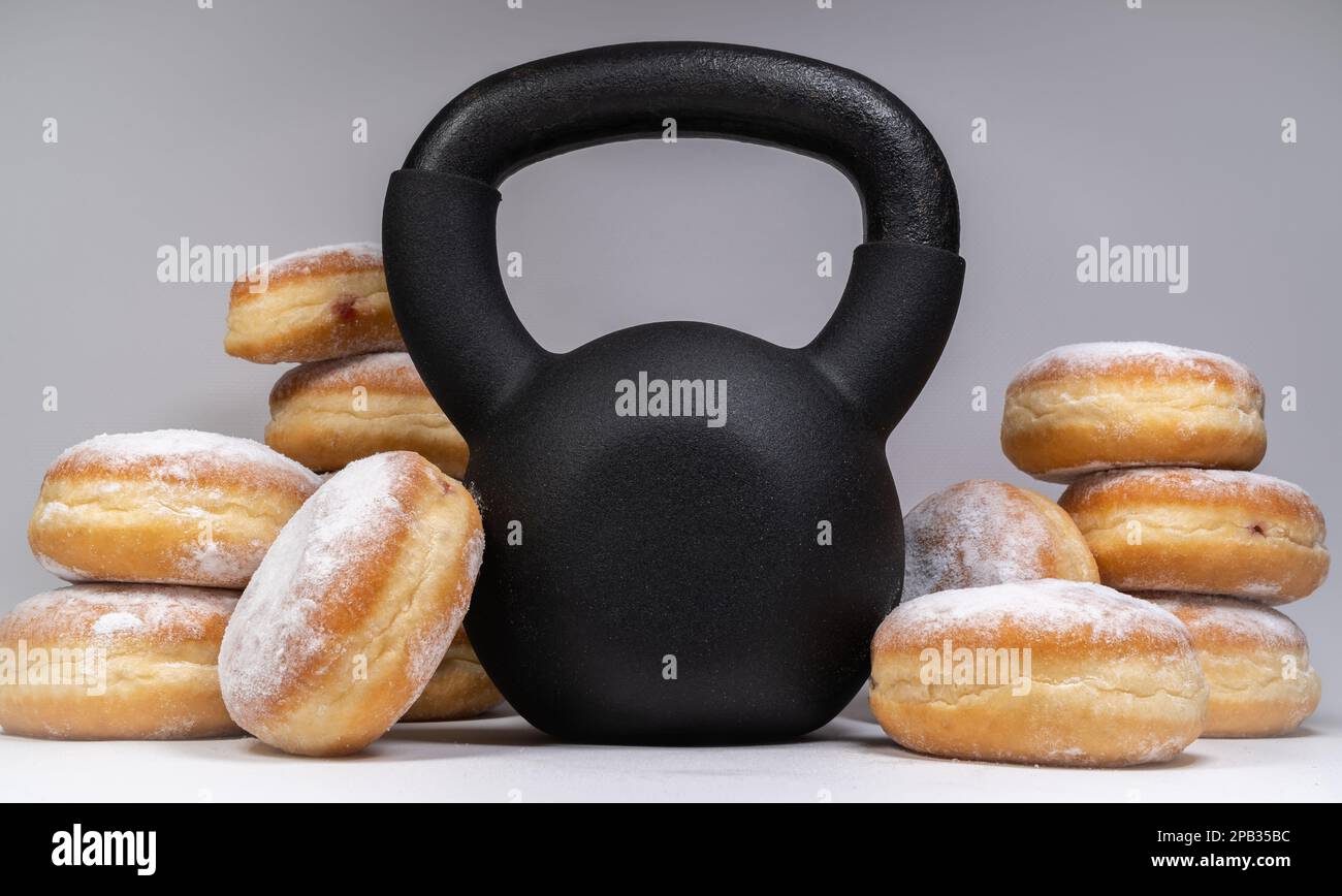 Gym kettlebell and Polish pączki deep-fried doughnuts. Healthy diet choice for Fat Thursday. Pączek feast day in Poland. Weight loss workout concept. Stock Photo