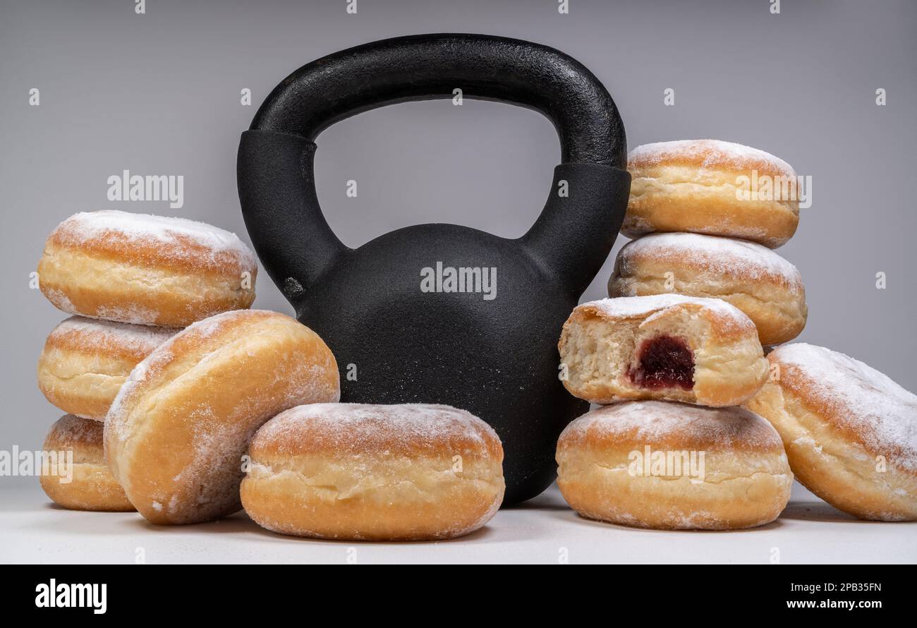 Gym kettlebell and Polish pączki deep-fried doughnuts. Healthy diet choice for Fat Thursday. Pączek feast day in Poland. Weight loss workout concept. Stock Photo