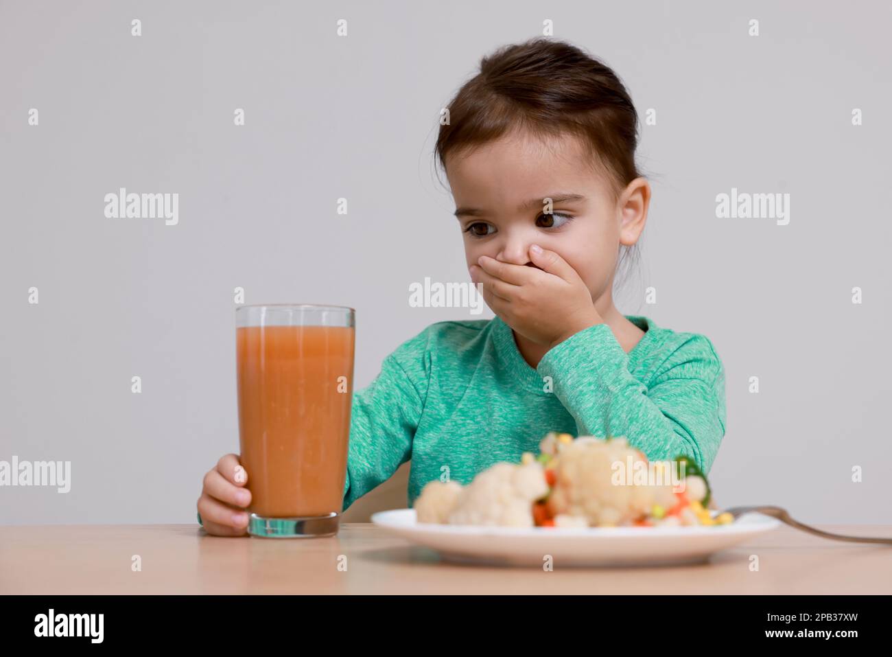 Refusing Tea Cute little girl covering mouth and refusing to drink juice at table on ...