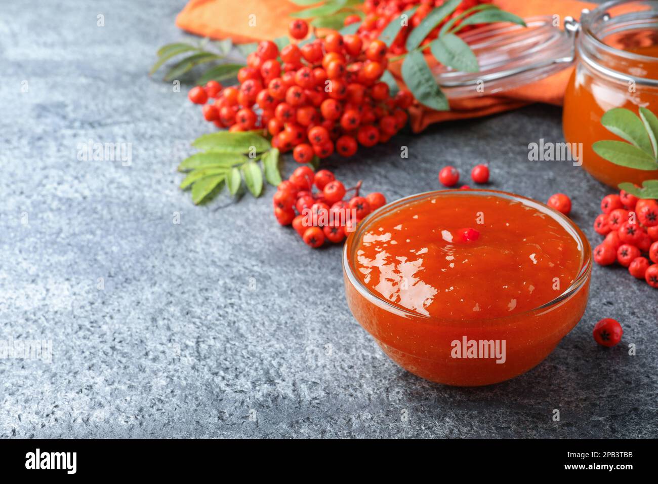 Delicious rowan jam in glass bowl and berries on grey table. Space for text Stock Photo