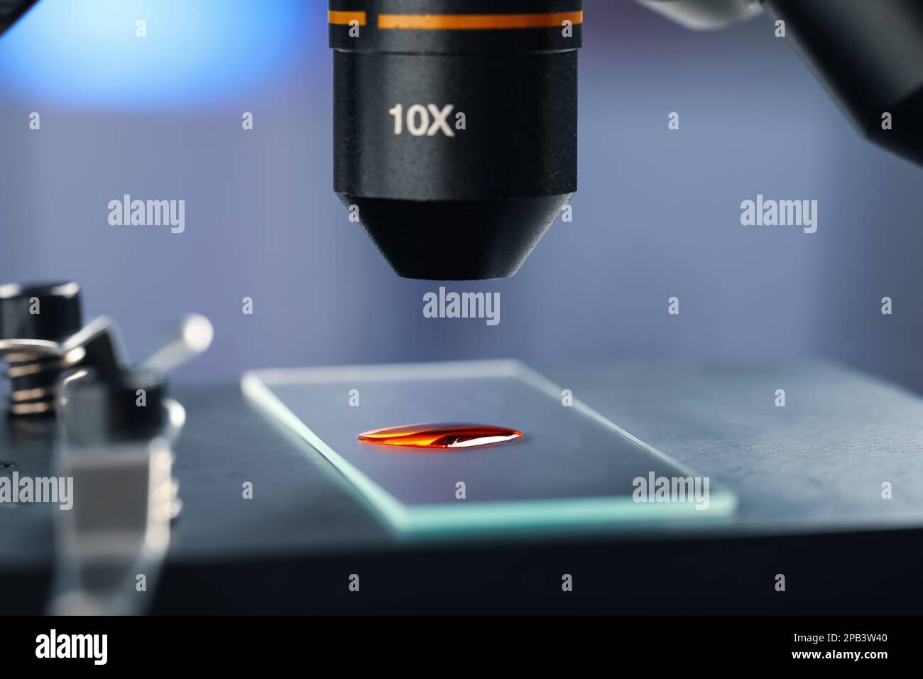 Glass slide with sample of red liquid under microscope in laboratory