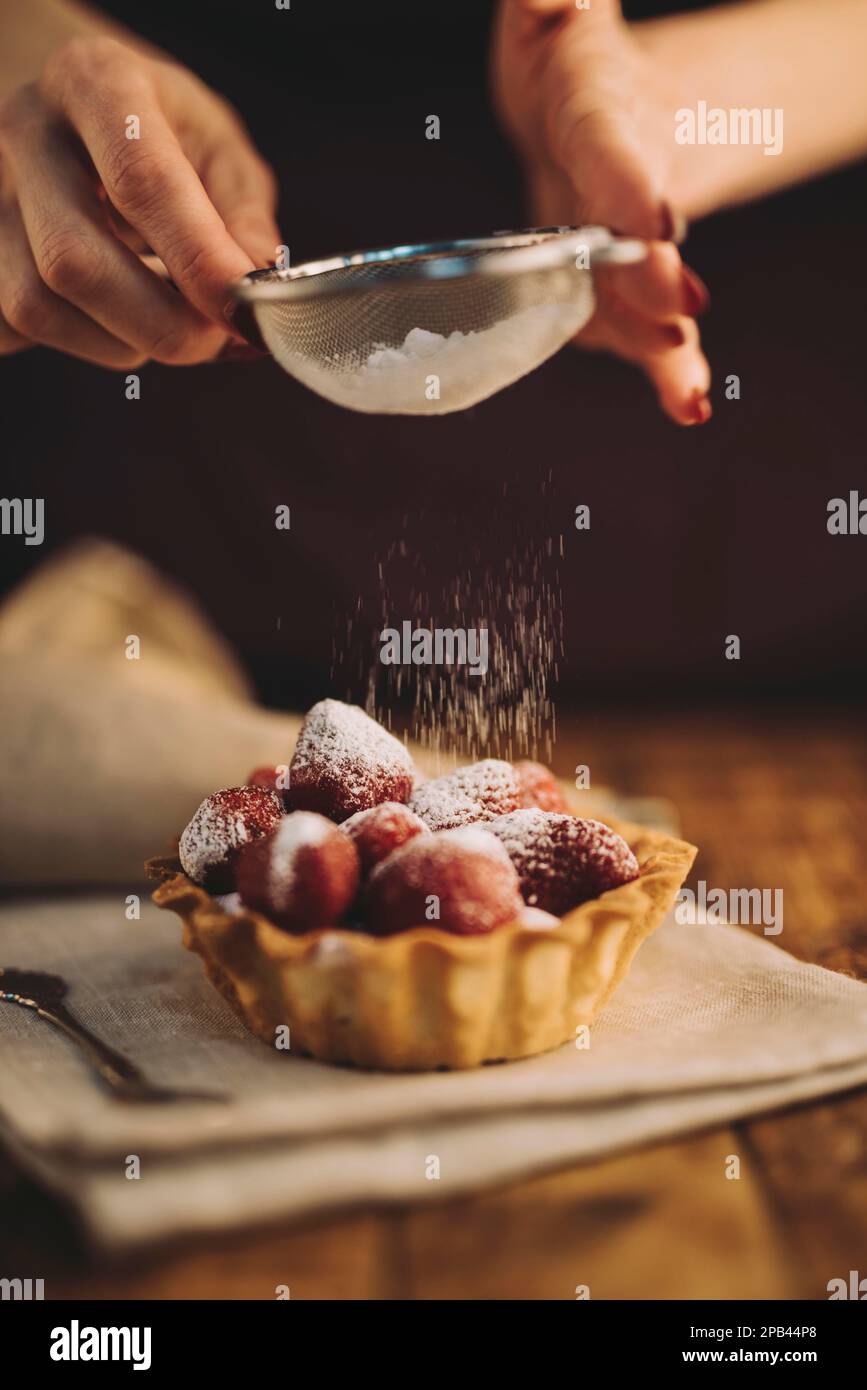 woman dusting sugar powder strawberry tart. High resolution photo Stock