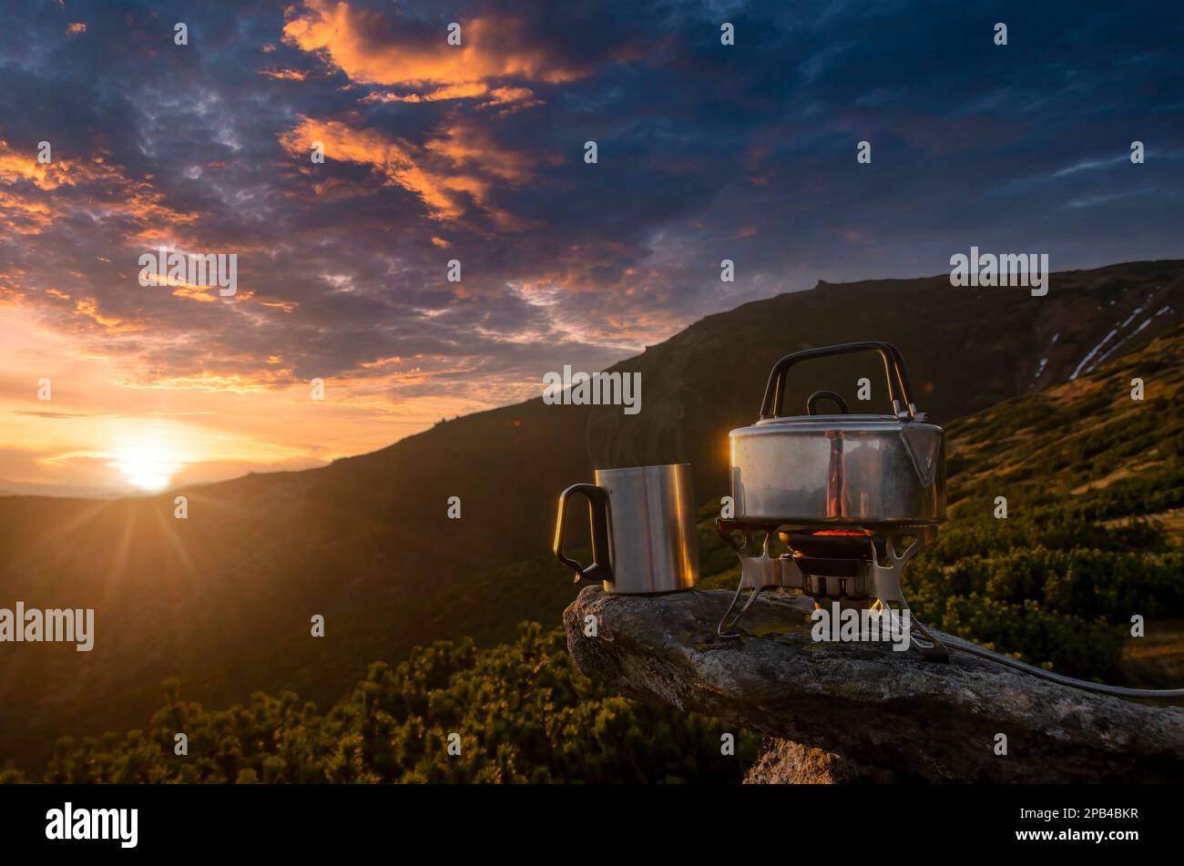 Cup of hot tea on the mountain top. Amazing mountain sunset with tourist stove, boiling teapot and a cup of tea. Symbol of vacation, freedom, outdoor Stock Photo