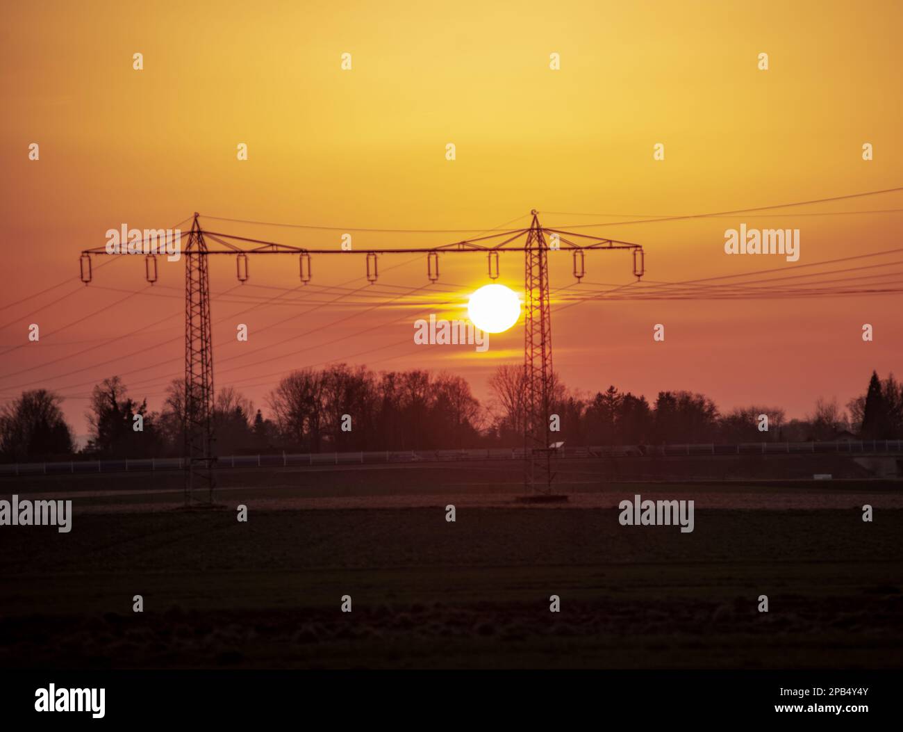 The sun sets between powerlines over fields. Stock Photo