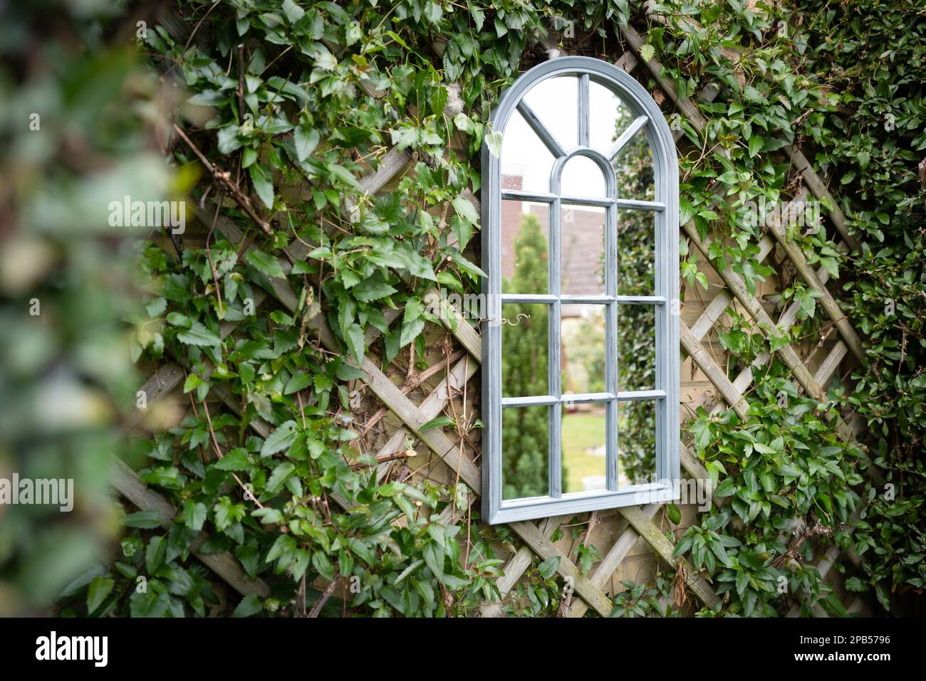 Shallow focus of a secret garden showing a ornate mirror seen attached to a trellis with vines growing around the frame. Stock Photo