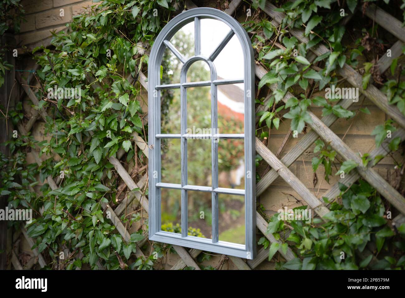 Shallow focus of a secret garden showing a ornate mirror seen attached to a trellis with vines growing around the frame. Stock Photo
