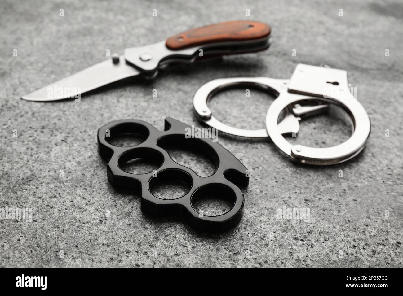https://c8.alamy.com/comp/2PB57GG/brass-knuckles-handcuffs-and-knife-on-grey-background-2PB57GG.jpg