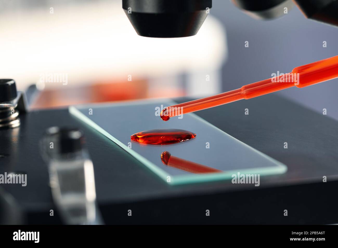 Dripping sample of red liquid onto slide under microscope in laboratory