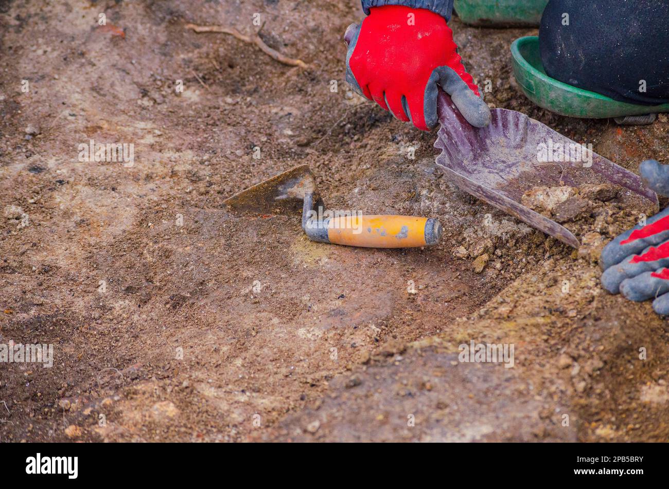 A hand of an archaeologist holding a charcoal-filled container and a trowel lying on the ground. Working archeology Stock Photo