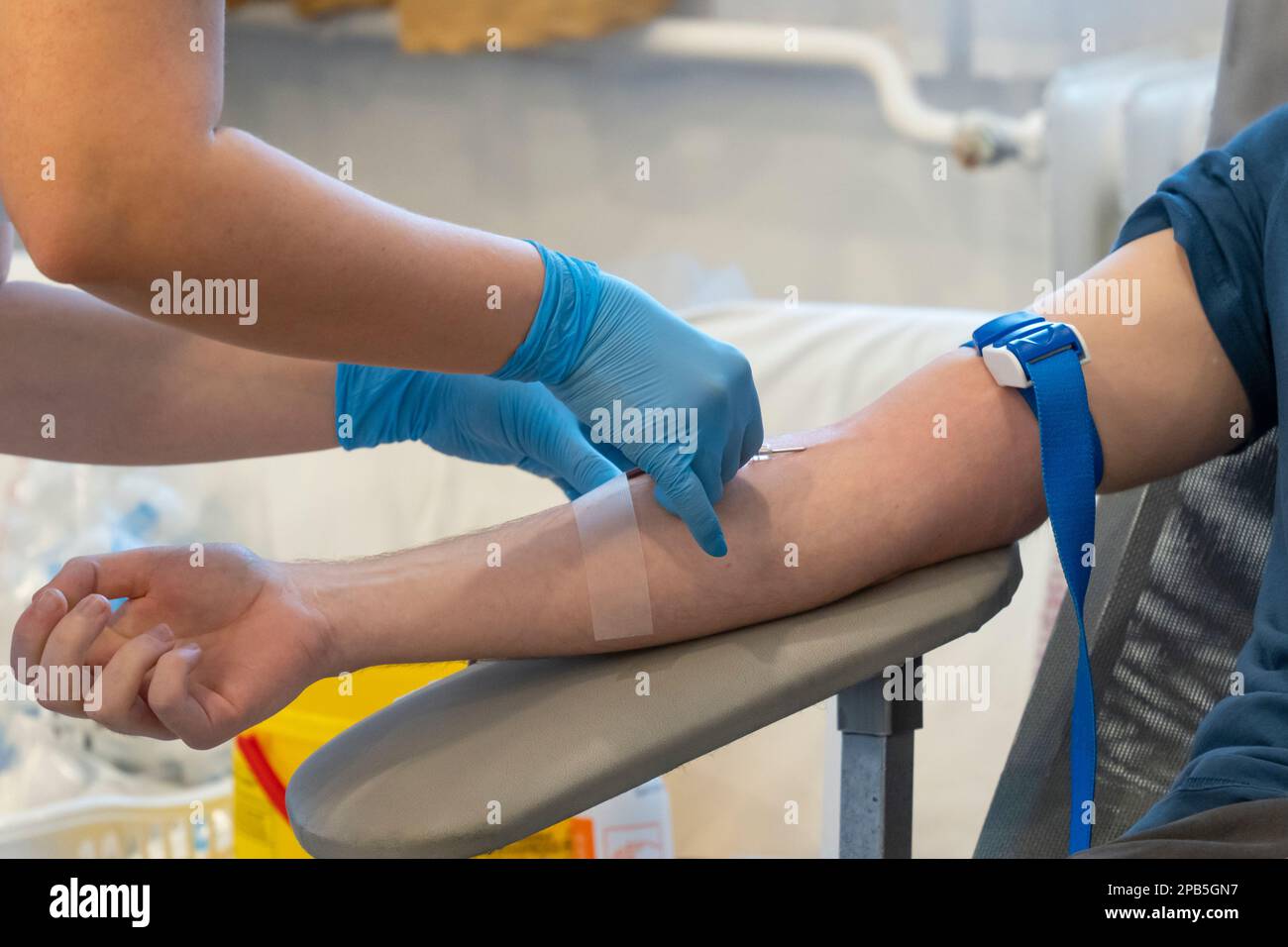 A nurse in blue gloves inserts a needle to take blood. Blood donation Stock Photo