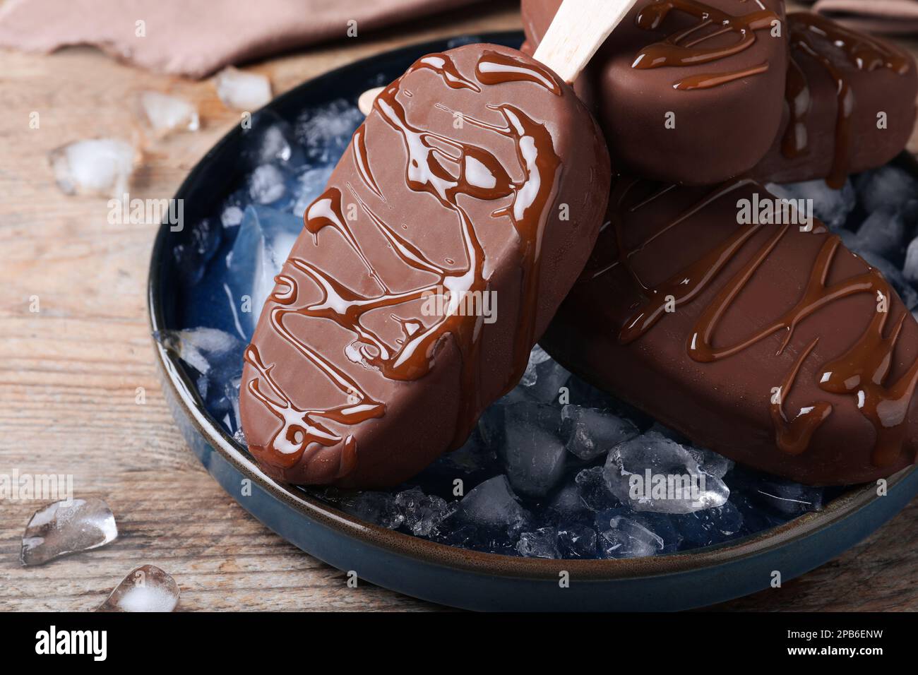 Delicious glazed ice cream bars and ice cubes on wooden table, closeup Stock Photo