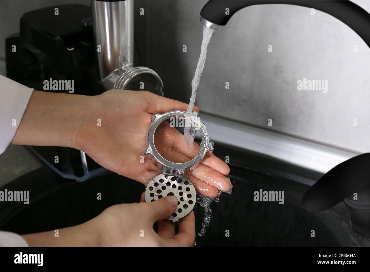 Woman washing parts of electric meat grinder under tap water in kitchen