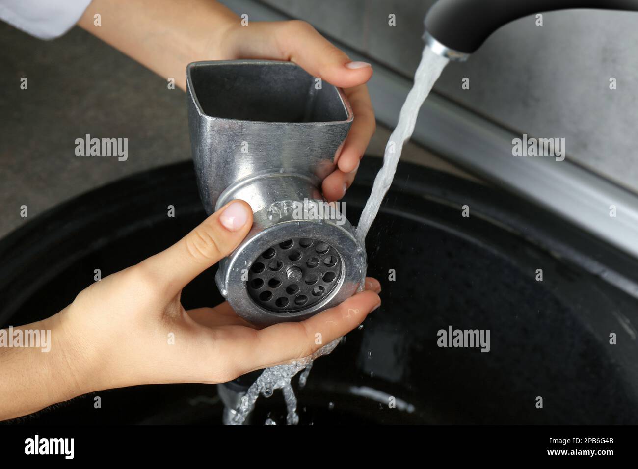 Woman washing manual meat grinder under tap water in kitchen sink
