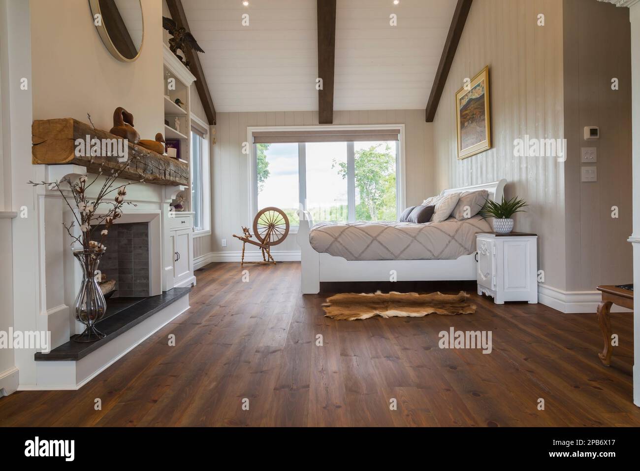 White painted king size sleigh bed in main bedroom with decorative fireplace, brushed wood plank walls, red pine wood floorboards inside timber home. Stock Photo