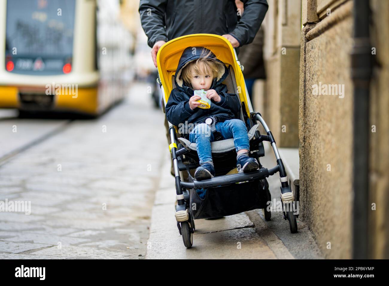 Young father and his toddler son in a stroller walking together down