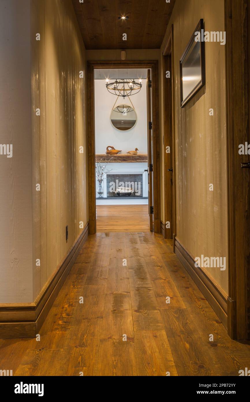 Hallway with brushed wood plank walls and red pine wood floorboards leading to main bedroom inside hybrid timber frame home. Stock Photo