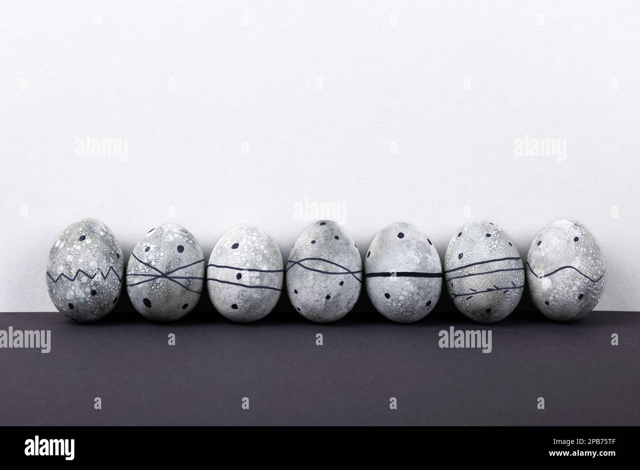 Seven grey Easter eggs in a black pattern on a grey background. Stock Photo