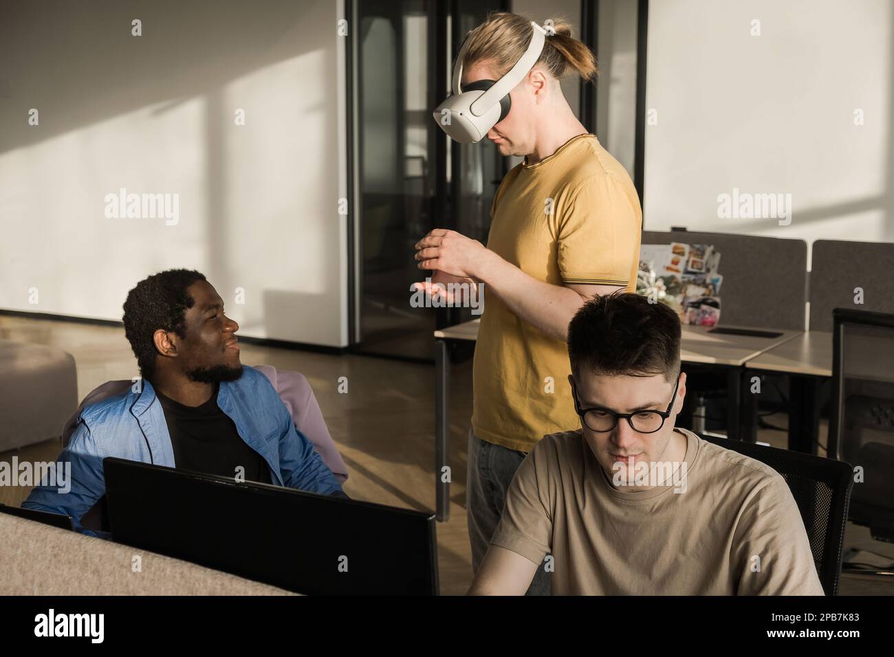 IT Development Team Working on VR Project. Man wearing VR headset, playing and touching something in the virtual world. Diverse men programmers using Stock Photo