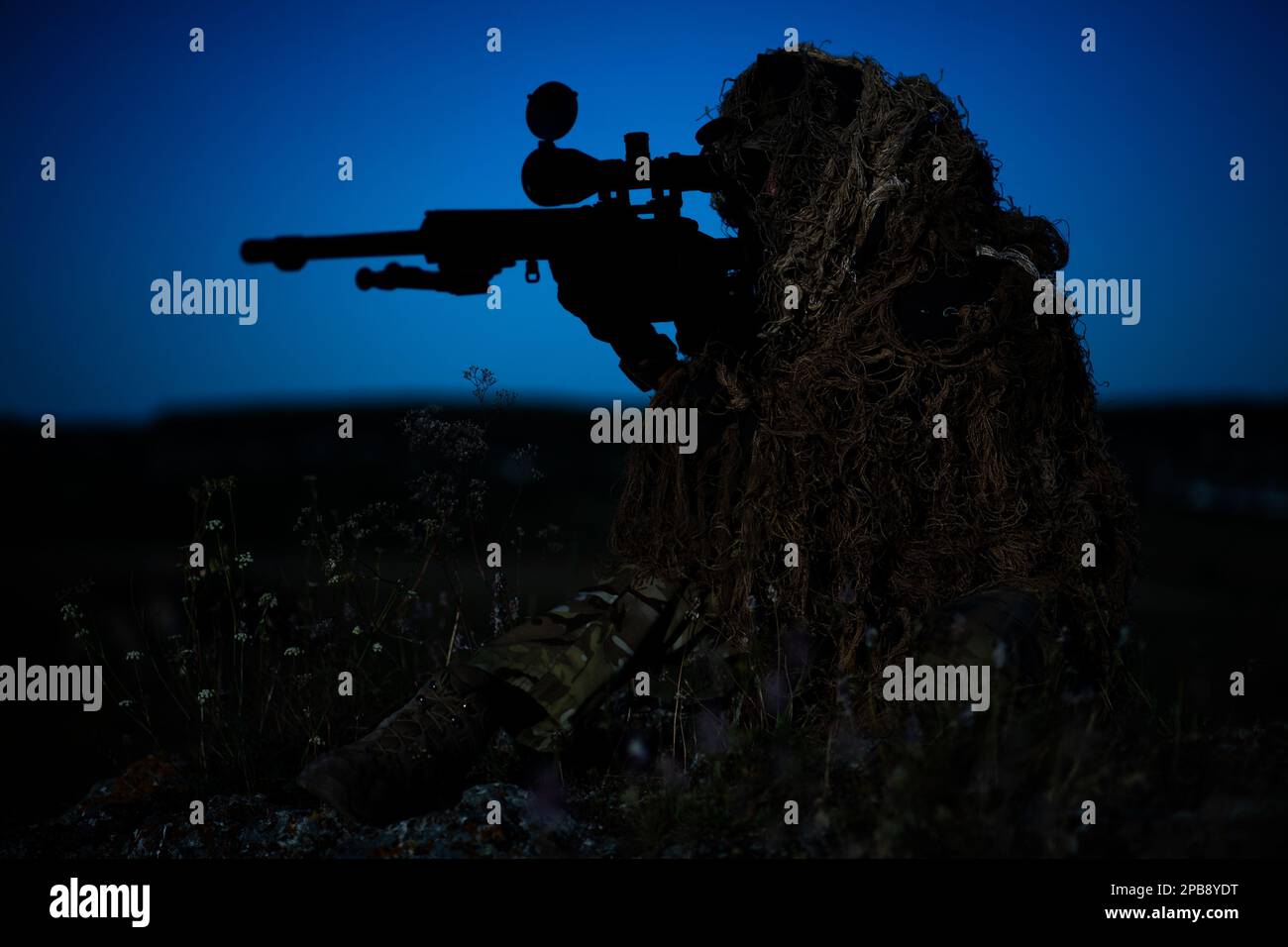 special operation forces sniper in ghillie (camouflage) suit with a high-precision rifle with optic scope in a combat position in the mountains at nig Stock Photo