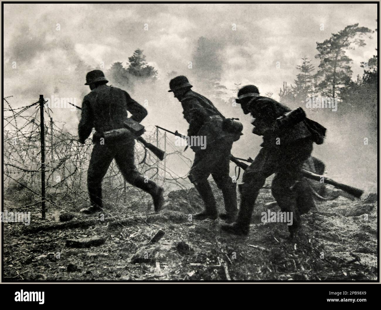 ARDENNES WW2 Nazi Soldiers under fire. German battlefield advance: Nazi Wehrmacht German troops under allied French fire advancing through a barbed wire battlefield front. Ardennes France. 1940s World War II Second World War Stock Photo