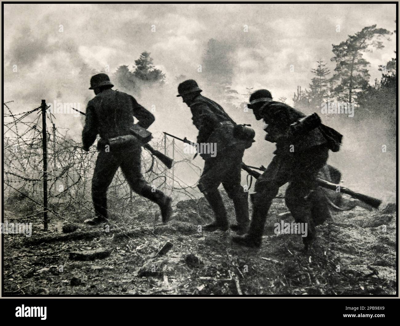 WW2 Nazi Soldiers under fire. German battlefield advance: Nazi Wehrmacht German troops under allied French fire advancing through a barbed wire battlefield front. Ardennes France  photographed by war reporter: Jager. 1940s World War II Second World War Stock Photo