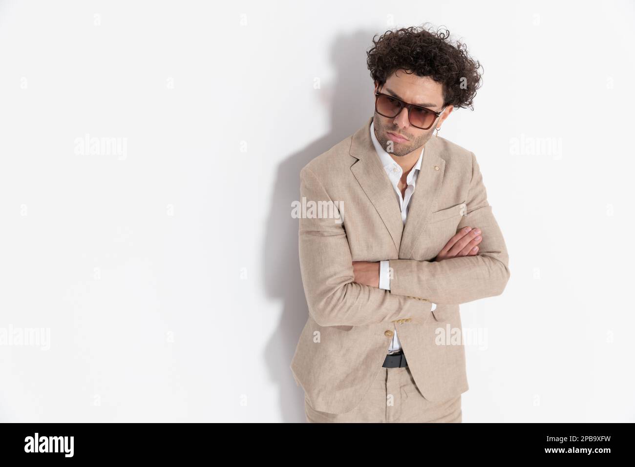 attractive man in beige suit with curly hair crossing arms and looking ...