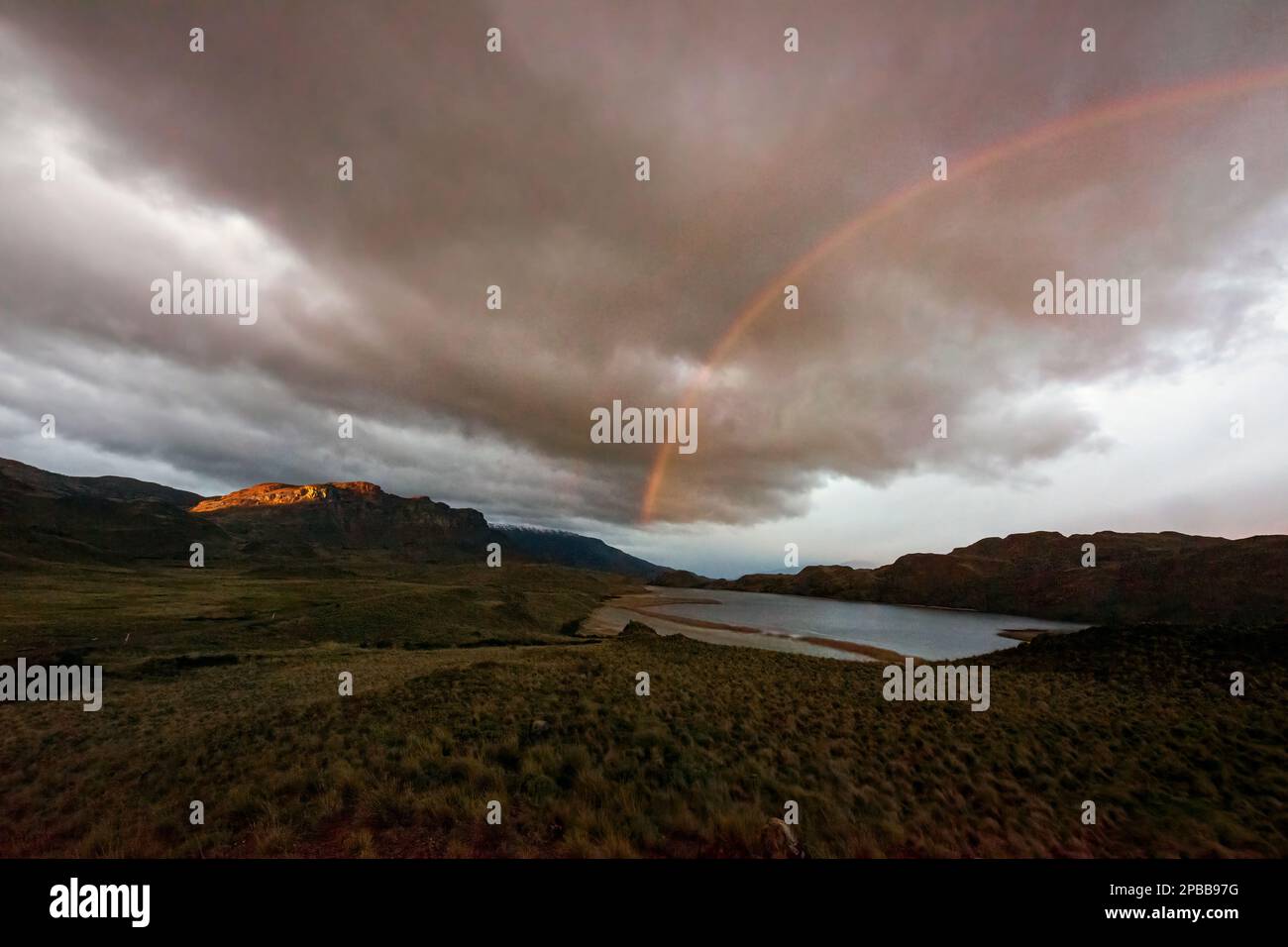 Rainbow with storm clouds and sunrise hitting cliff, Valle Chacabuco, Patagonia Stock Photo