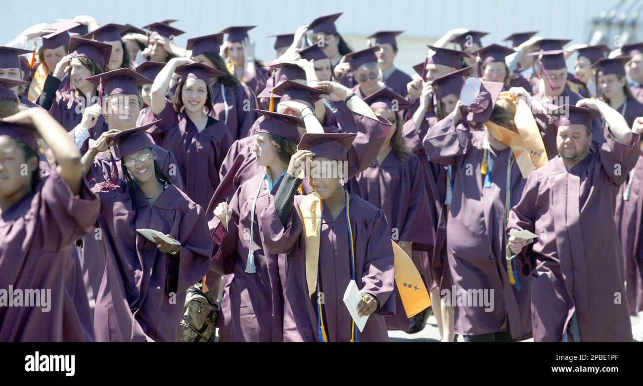 Olympic College graduates hold onto their caps as a gust of wind hits them as they are in the