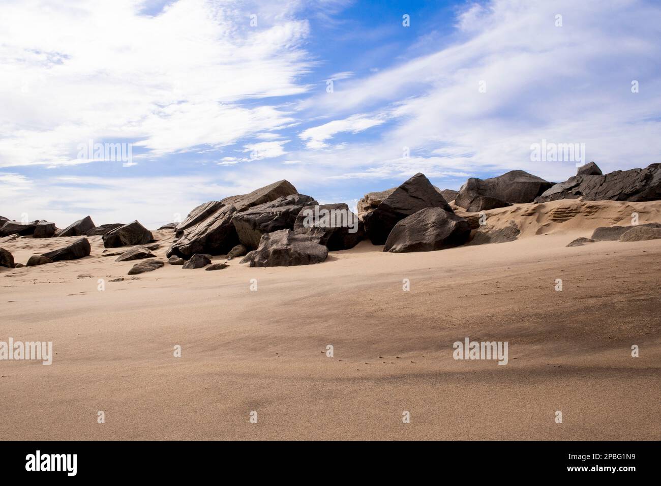 Sandy beach with boulders, rocks. Blue sky, wispy clouds on a winter's day, Sandy Hook Beach, New Jersey, part of Gateway National Recreation Area. Stock Photo