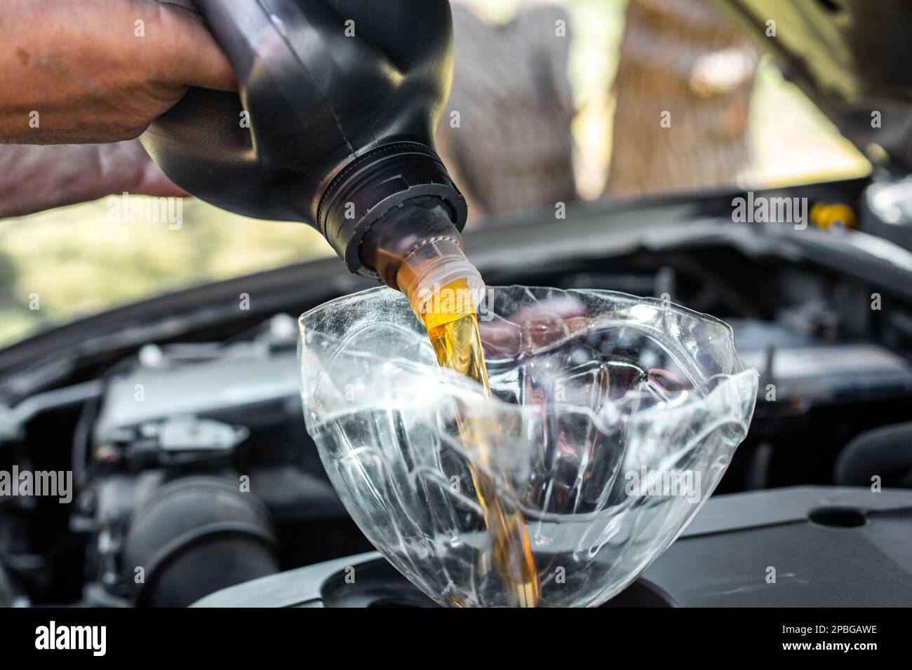A man is pouring machine oil into a car engine through a homemade