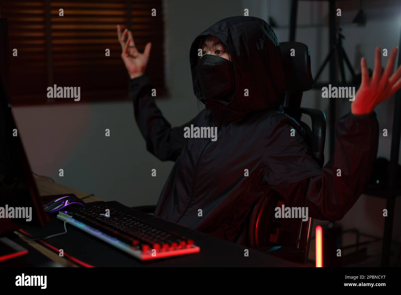 Hacker in hoodie raising hands while having problem with hacking programming system or server. Stock Photo