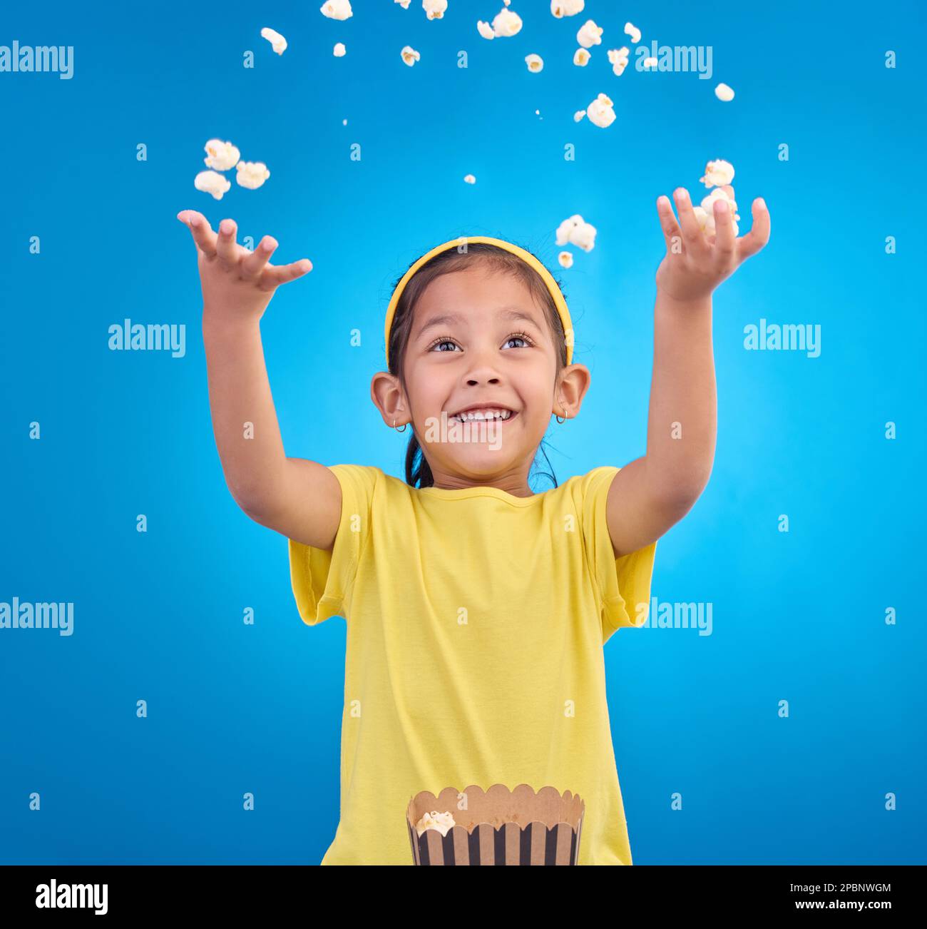 Food, happy and child throw popcorn on blue background for entertainment, movies and cinema mockup. Comic, smile and excited young girl with sweet Stock Photo