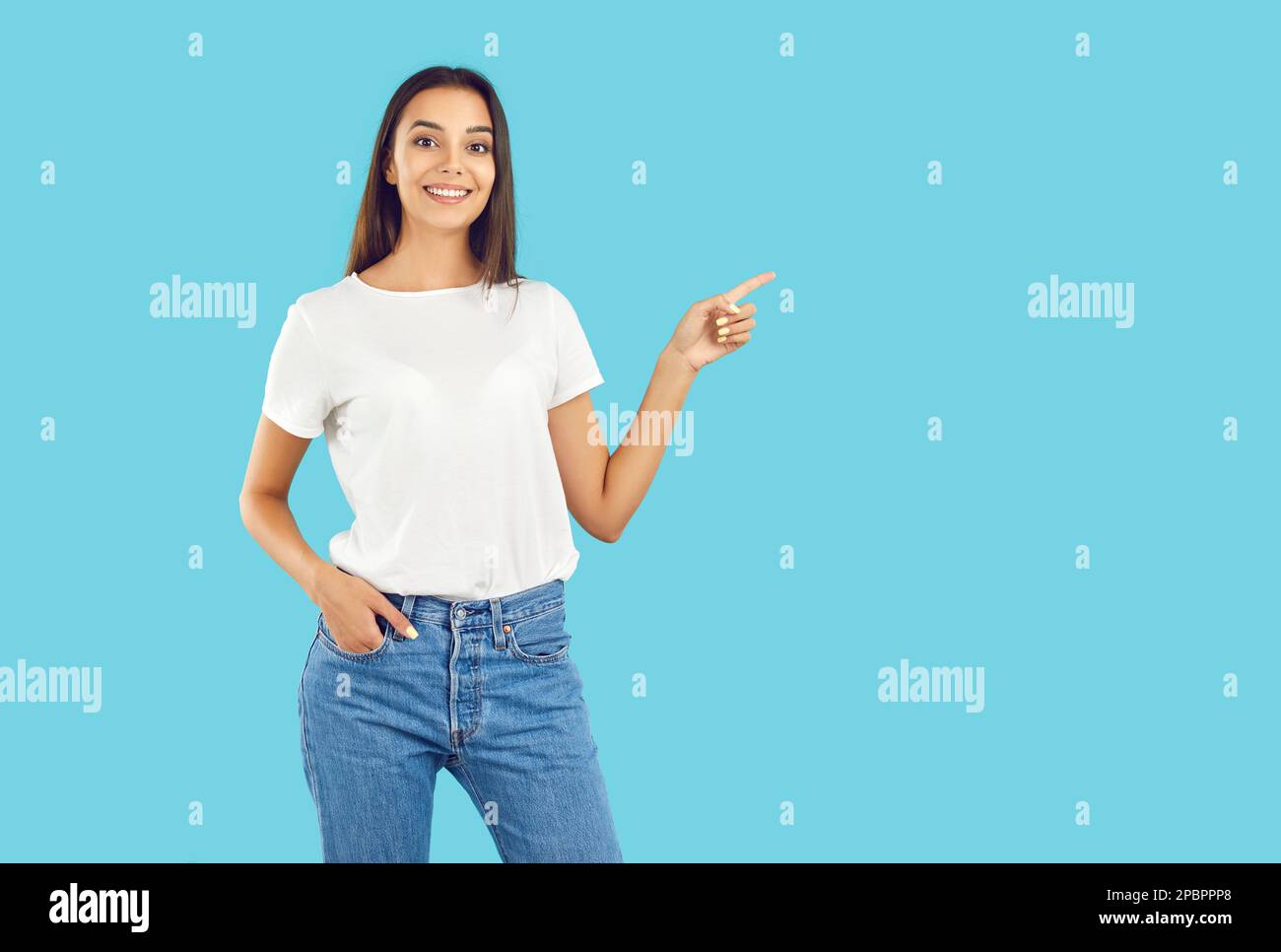 Happy young woman in T shirt and jeans pointing at copy space side on blue background Stock Photo