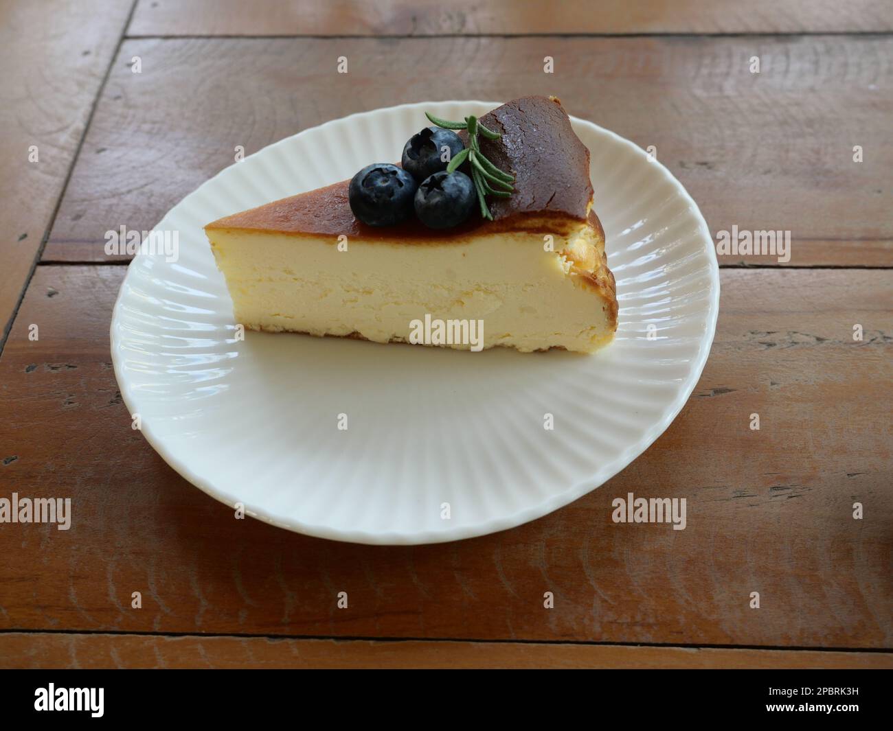 Cheesecake pie slice topped with blueberry fruit on a plate, Sweet food with brown table in background Stock Photo