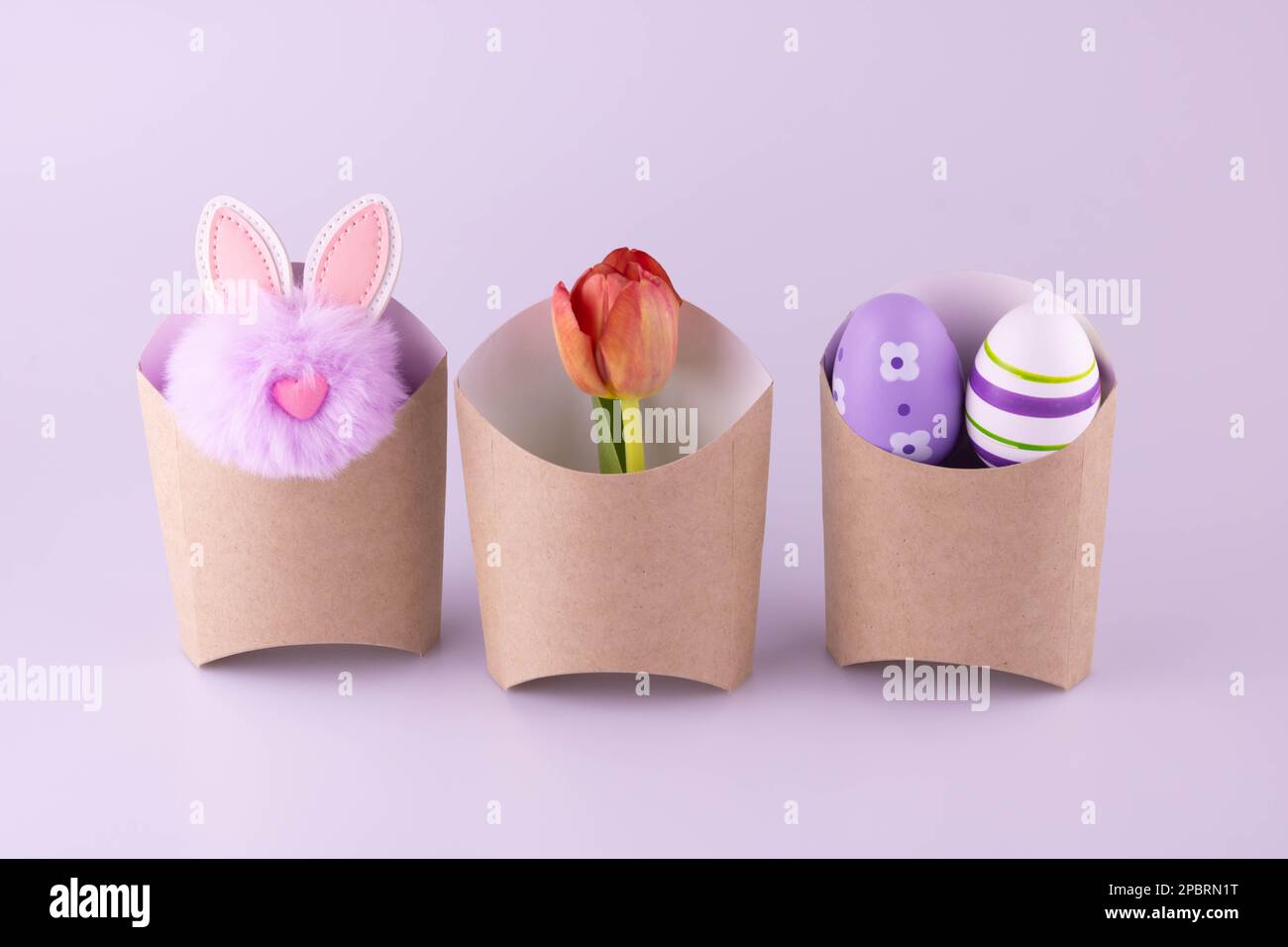 Paper bags with a cute lilac rabbit, tulip and eggs on a pink background.The concept of Easter. Zero waste and environmentally friendly concept. Stock Photo