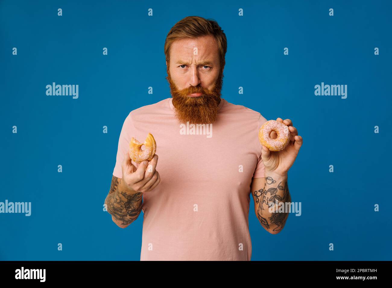 Upset bearded white man in casual wear holding donuts isolated over blue wall Stock Photo