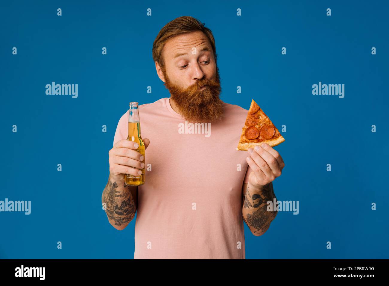 Portrait of confused white man choosing between pizza and beer apple isolated over blue background Stock Photo