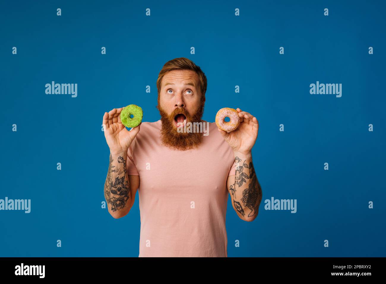 Bearded excited man holding donuts while standing isolated over blue background Stock Photo