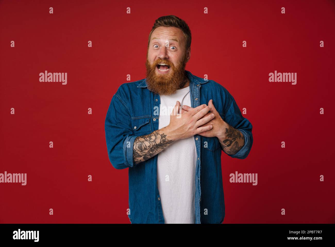 Adult redhead bearded tattooed man dwith opened mouth and folded hands ...