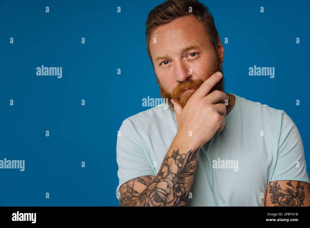 Adult redhead bearded tattooed thoughtful man in t-shirt holding his ...