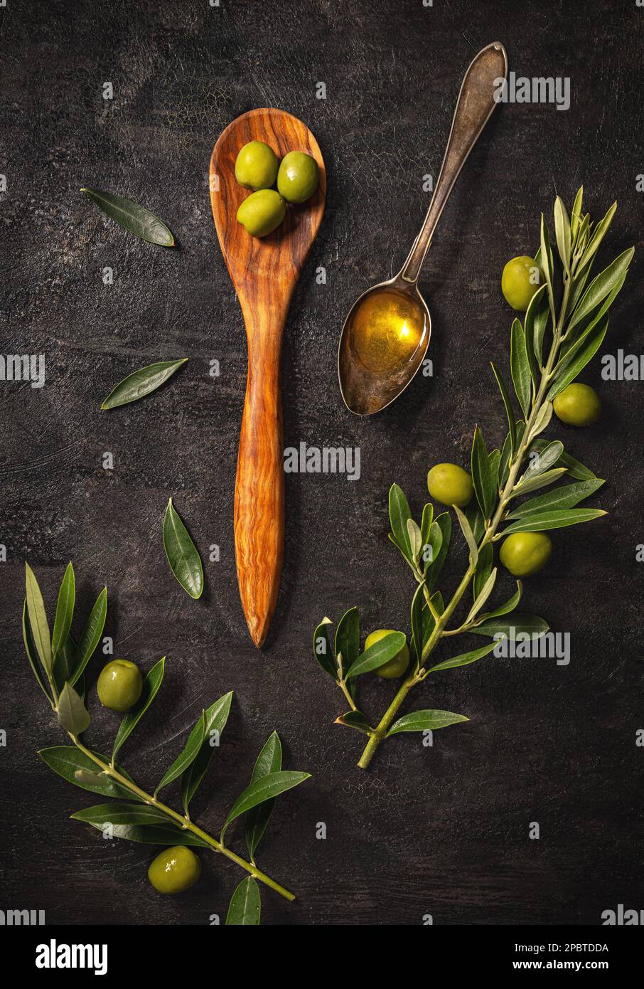 Flat lay of olive branch, olives and spoon of olive oil on black slate